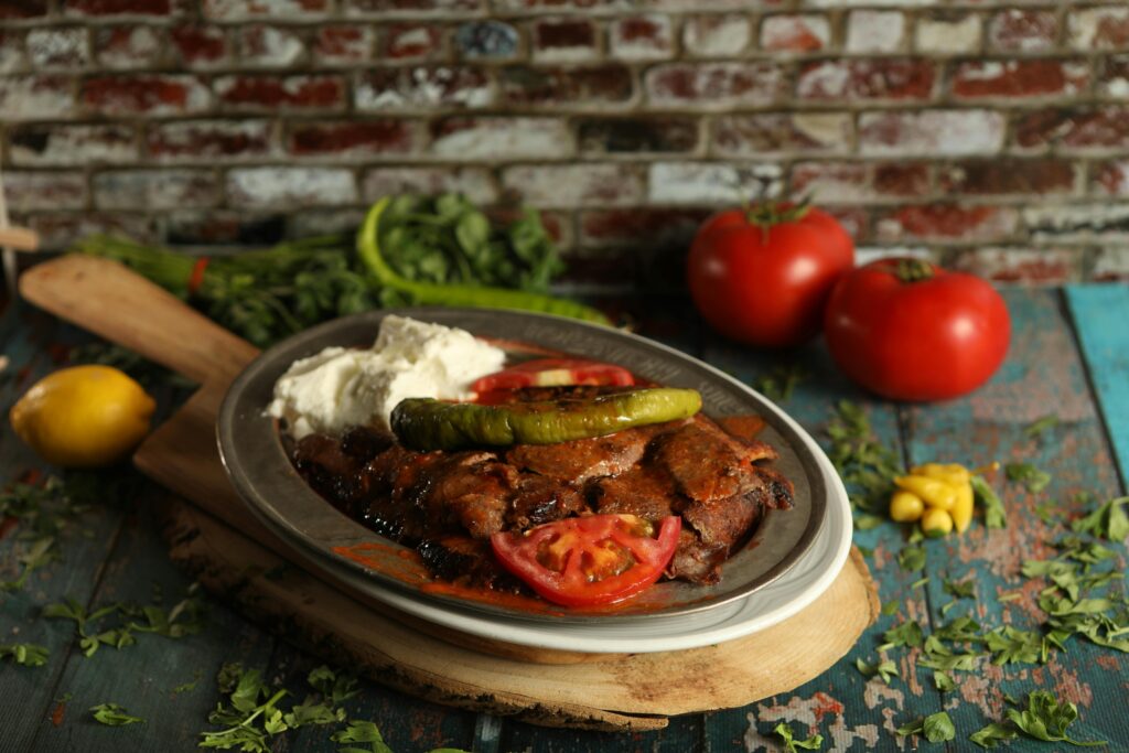 İskender Kebap (Turkish Döner with Yogurt and Tomato Sauce) Delicious Iskender kebab served with vegetables on a rustic table setting, perfect for food lovers.