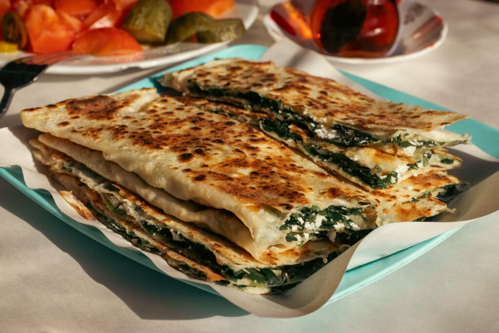 Gözleme (Turkish Stuffed Flatbread) Close-up of freshly made Turkish Gözleme with spinach and cheese on a plate outdoors.